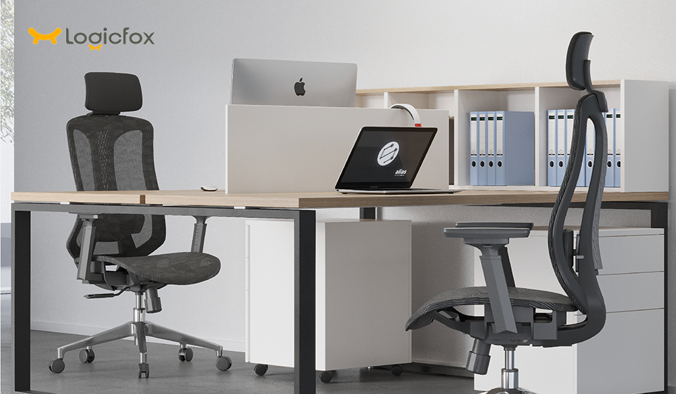 A picture of 2 black mesh ergonomic chairs, with a computer on the desk. 